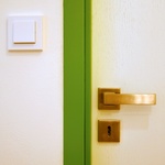 Detail kování ložnicových dveří a vypínače ABB v kontrastu se zelenou kovovou zárubní, která nahradila zárubeň původní