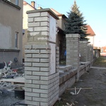 Původní elektro kiosek byl standardizovaně postaven z bílých cihel. Abychom sjednotili jeho vzhled se zbytkem betonových sloupků, resp. s podobu celého plotu, byl obložen dutými betonovými cihlami, které šikovný zedník rozřezal na jednotlivé segmenty, kterými celý sloupek postupně obložil. Iluze je dokonalá, nový elektro kiosek je od nově vyzděných betonových sloupků k nerozeznání.