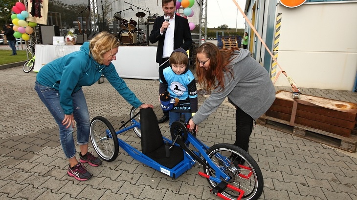 Osmiletý Michal Novotný nasedá na darovaný handbike od Lindabu za asistence své maminky (vpravo), marketingové manažerky Lindabu Petry Ždánské (vlevo) a moderátora akce – herce a režiséra Ondřeje Sokola.